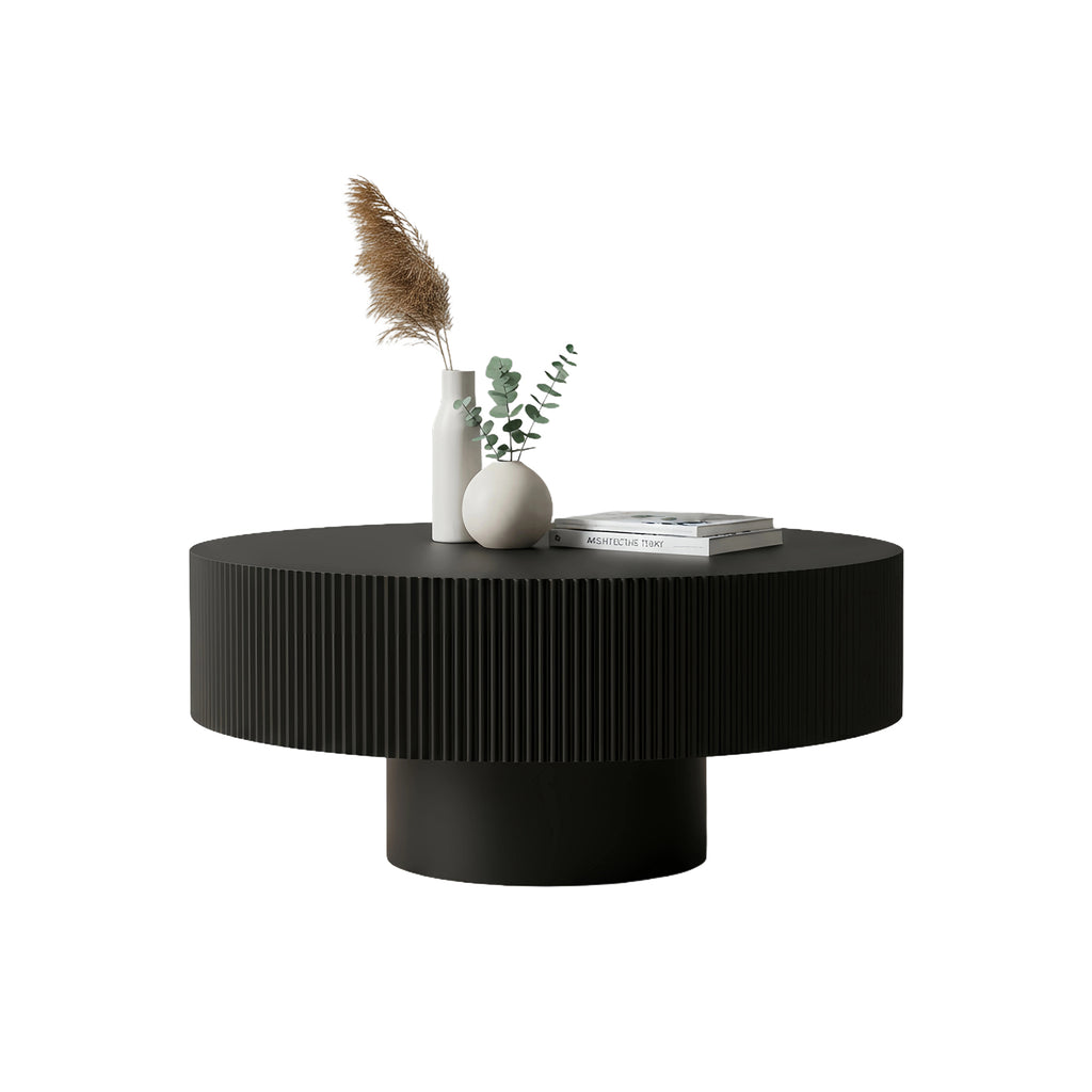 Black fluted drum coffee table styled with a vase and books on a white background
