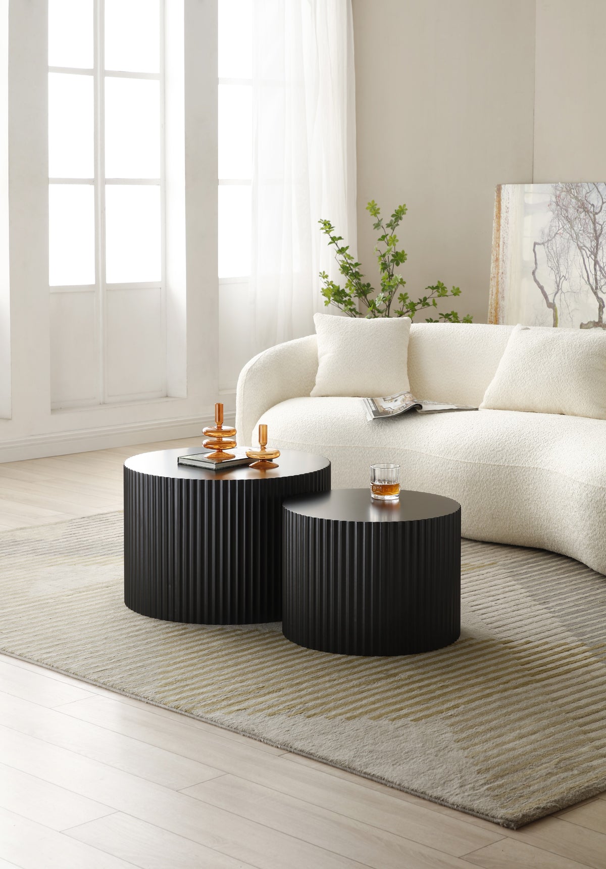 Two black fluted drum tables clustered before a cream boucle sofa in a sunlit room