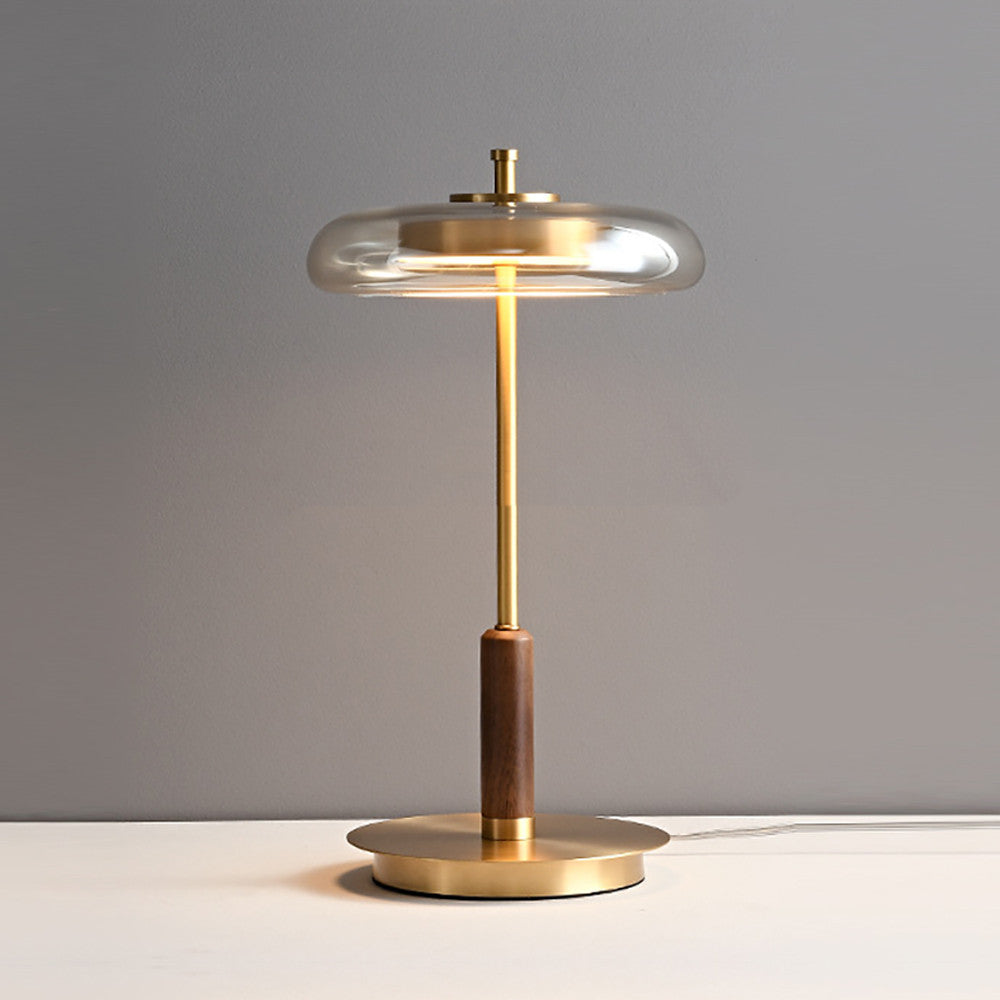 Glass disc table lamp with walnut grip, lit, on a white surface — full view with cord