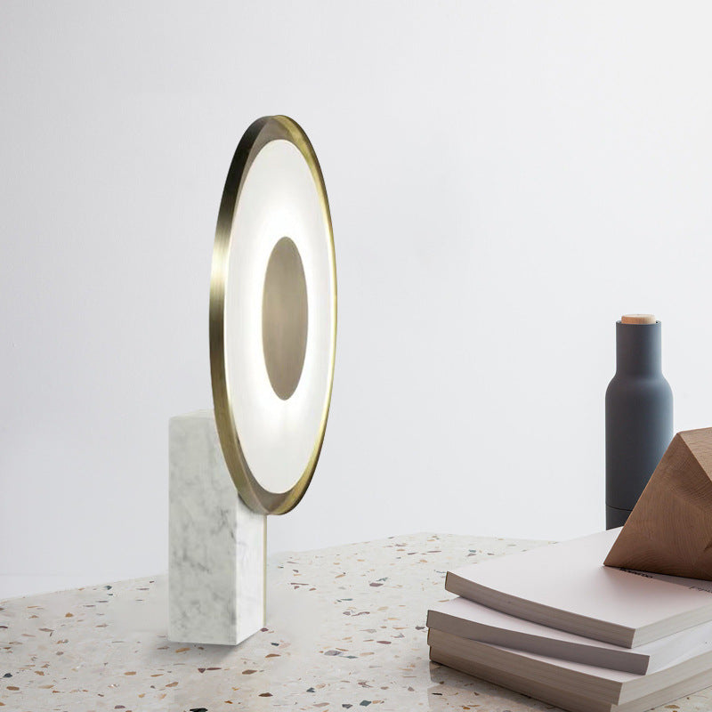 Halo ring table lamp in side profile on a terrazzo surface beside stacked books