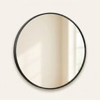 Round wall mirror with slim black metal frame on a warm cream background