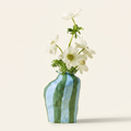 Striped ceramic flower vase in glossy blue and green on a warm cream background