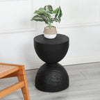 Black hourglass side table holding a potted plant beside a wooden cane chair