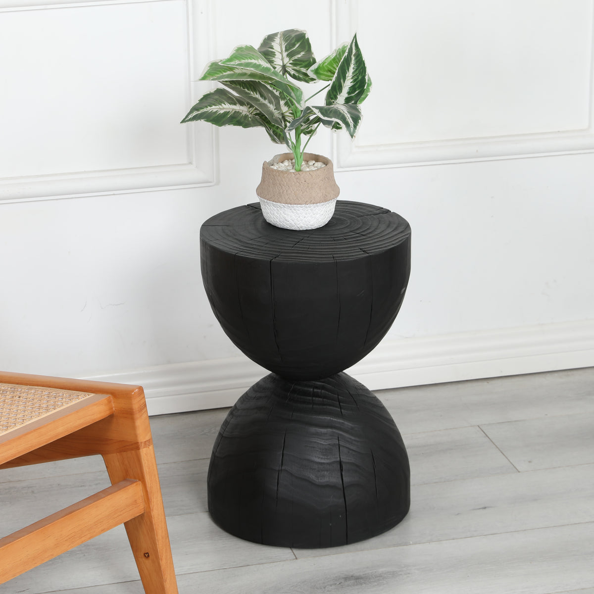 Black hourglass side table holding a potted plant beside a wooden cane chair