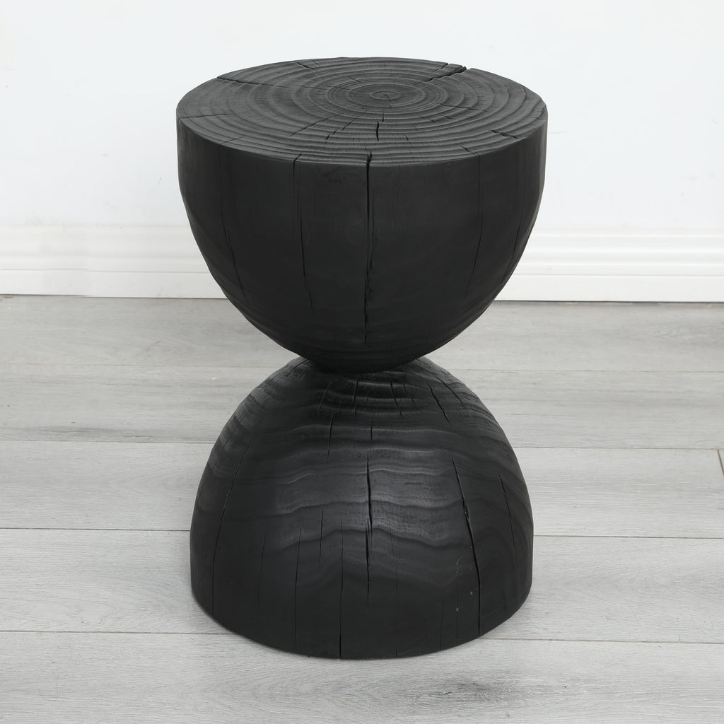 Burnt mango wood hourglass side table on a pale grey wood floor against a white wall
