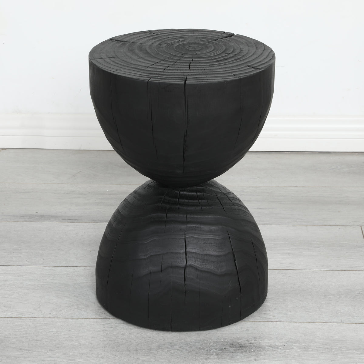 Burnt mango wood hourglass side table on a pale grey wood floor against a white wall
