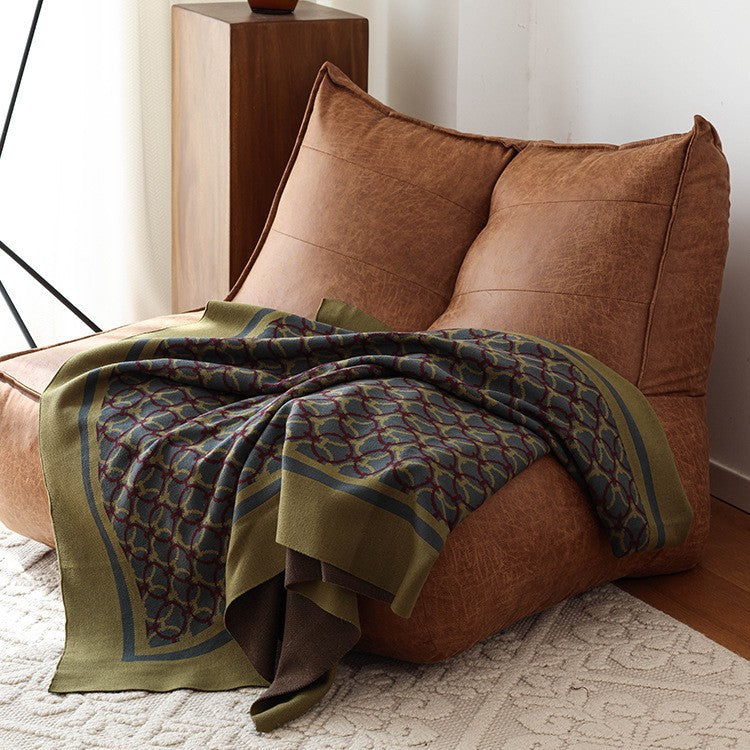 Olive knit throw blanket with ring pattern draped over a tan leather lounge chair