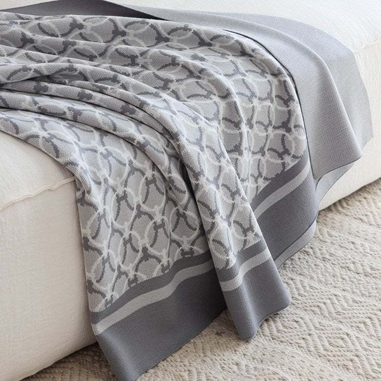 Light grey ring-pattern knit throw draped over a white sofa onto a cream rug