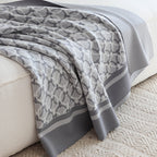 Light grey ring-pattern knit throw draped over a white sofa onto a cream rug