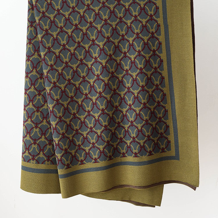 Olive knit throw blanket with interlocking ring pattern and wide border, hanging against a white wall