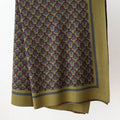 Olive knit throw blanket with interlocking ring pattern and wide border, hanging against a white wall