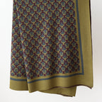 Olive knit throw blanket with interlocking ring pattern and wide border, hanging against a white wall