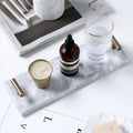 White marble vanity tray with brass-tone T-bar handles holding a candle, amber bottle and ribbed glass