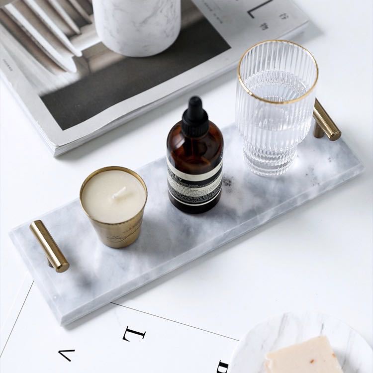 White marble vanity tray with brass-tone T-bar handles holding a candle, amber bottle and ribbed glass