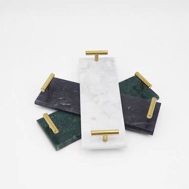Marble vanity trays with brass-tone T-bar handles in white, charcoal and emerald, overlapping on a plain white background