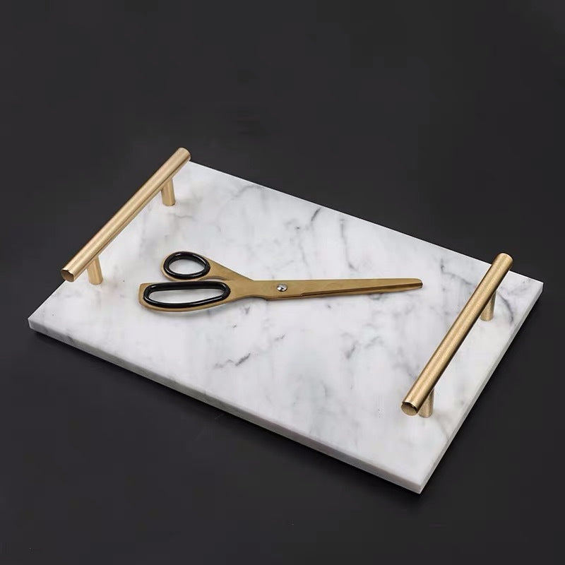 White marble vanity tray with gold-tone handles on a black surface, gold scissors on top