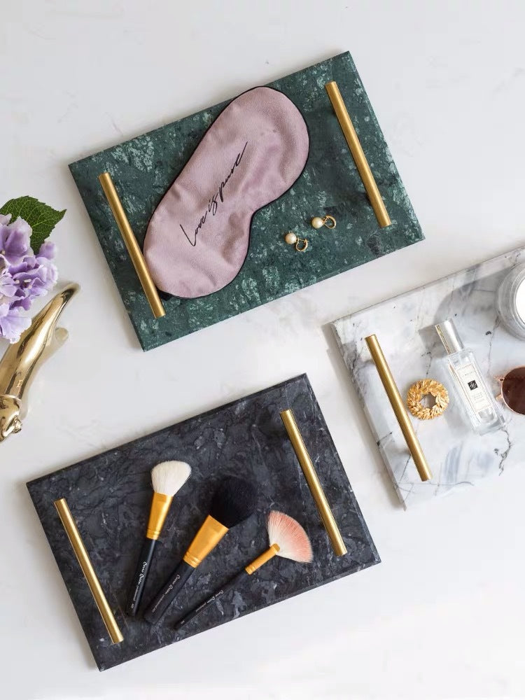 Green, black and white marble trays with gold-tone handles styled with a sleep mask and brushes