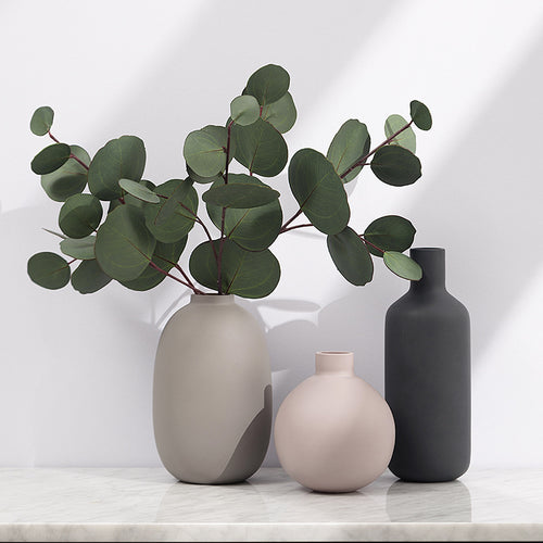 Matte ceramic bud vases in blush, taupe and charcoal on a marble shelf, the taupe oval holding eucalyptus