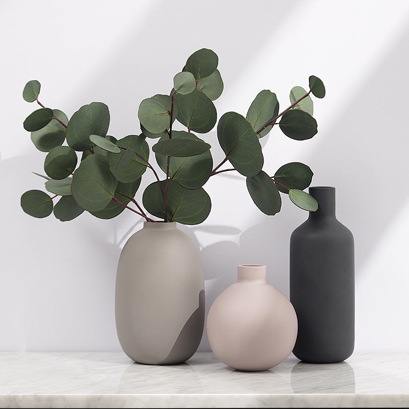 Matte ceramic bud vases in blush, taupe and charcoal on a marble shelf, the taupe oval holding eucalyptus