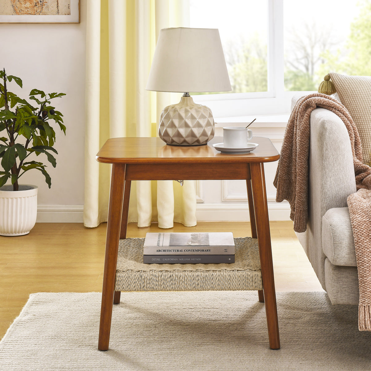 Mid-century side table with woven shelf holding books, beside a sofa with a throw