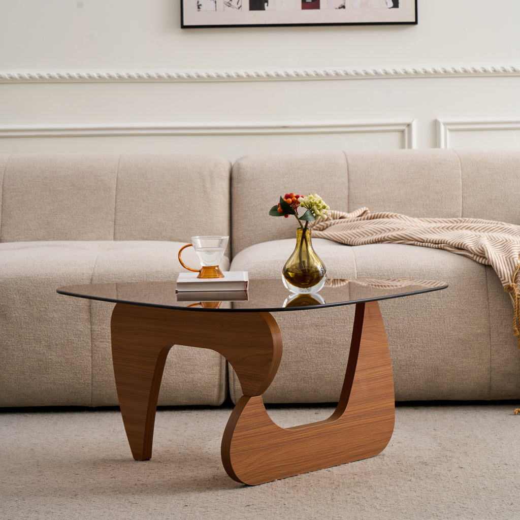 Tinted glass coffee table with curved base in front of a cream sofa, a vase and cup on top