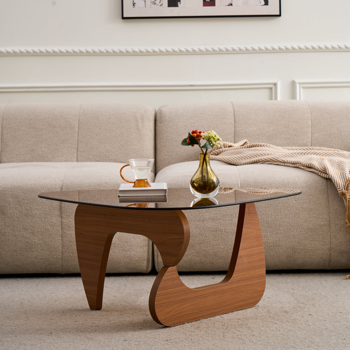 Tinted glass coffee table with curved base in front of a cream sofa, a vase and cup on top
