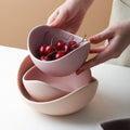 Lilac ceramic lotus bowls being lifted apart, the top bowl holding cherries