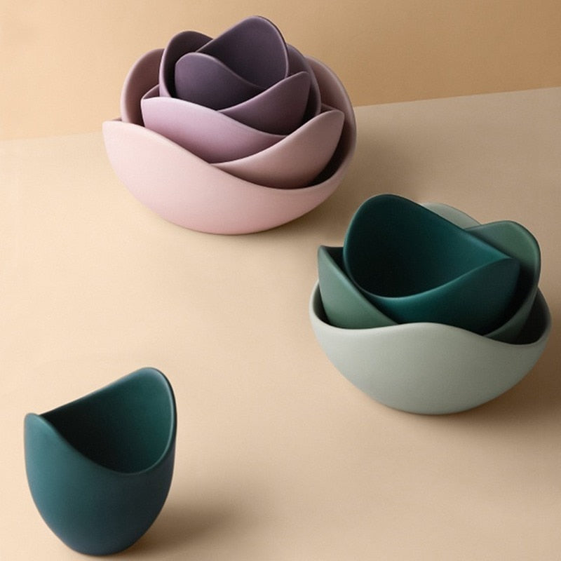 Lilac and sage matte ceramic lotus bowls stacked into flower shapes on a warm beige surface