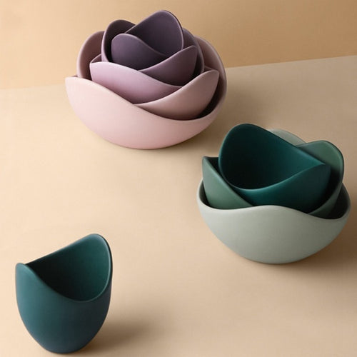 Lilac and sage matte ceramic lotus bowls stacked into flower shapes on a warm beige surface