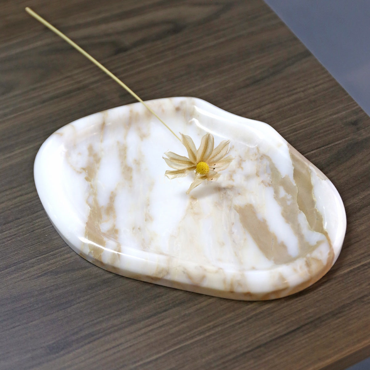 Pebble-shaped stone catchall tray in Gold, white marble with gold-toned veins, on a dark wood table