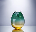 Pinched ombre glass vase in teal and amber turned to show the pressed dents, on a grey background