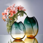 Pinched ombre glass vase in teal and amber styled with pink orchid stems beside a taller version of the design
