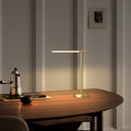 Brushed brass desk lamp with a level light bar, lit on a walnut desk against a pale paneled wall