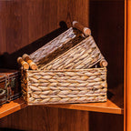 Two woven straw baskets with wooden handles nested on a corner shelf