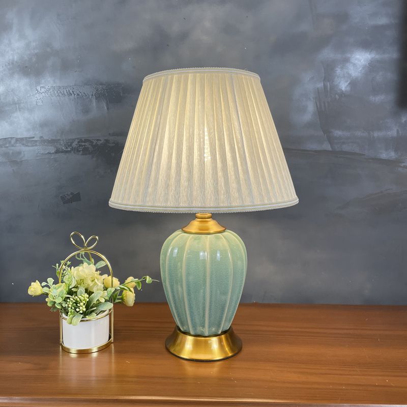Ribbed sage green ceramic table lamp with cream pleated shade beside a pot of flowers