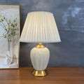 Ribbed cream ceramic table lamp with pleated shade on a wood sideboard against a dark wall