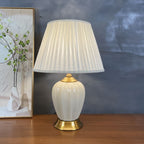 Ribbed cream ceramic table lamp with pleated shade on a wood sideboard against a dark wall