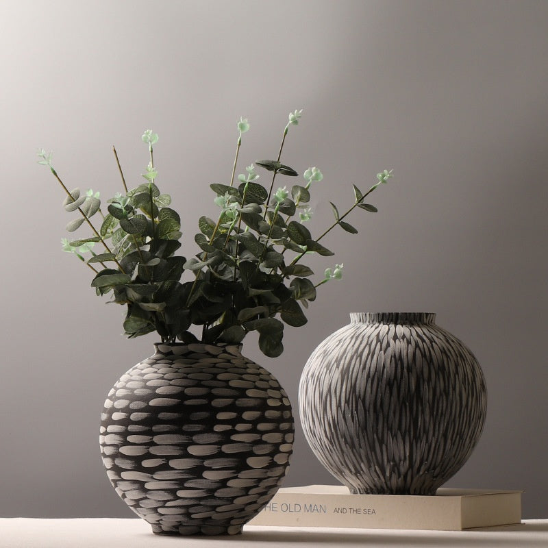 Horizontal dab ceramic vase holding faux eucalyptus beside the vertical feather style against a grey wall