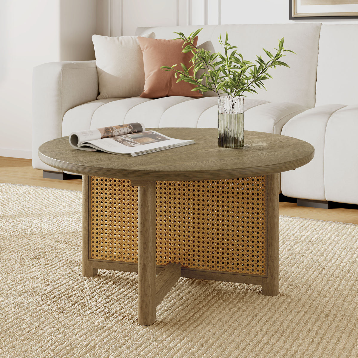 Round wood and cane coffee table on a cream rug before a white sofa, with a magazine and a vase of greenery