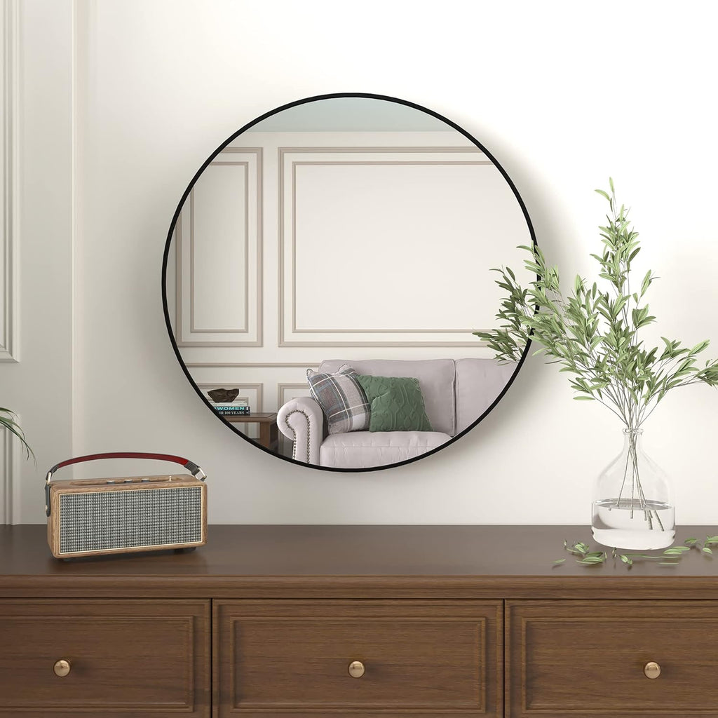 Large round black wall mirror above a walnut dresser with a vase of olive branches