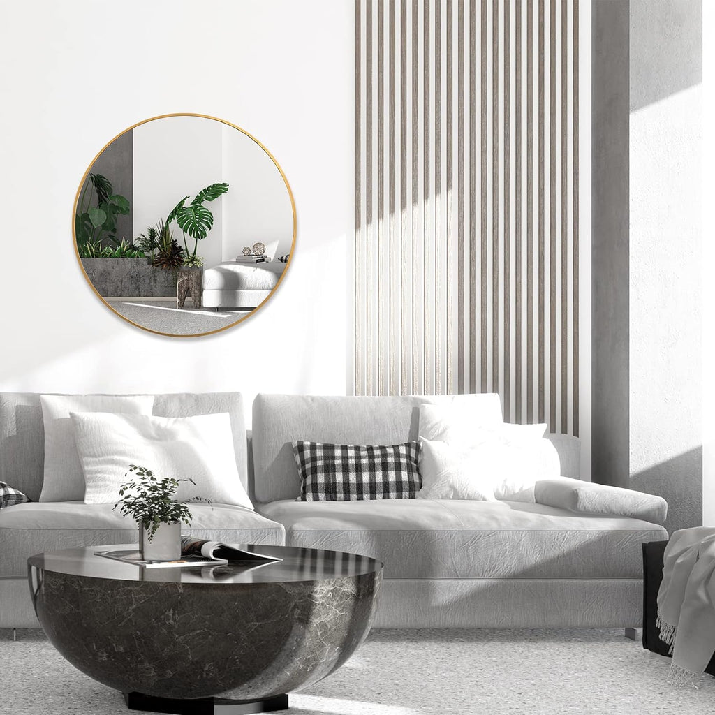 Round brushed gold mirror hung above a grey sofa in a white living room