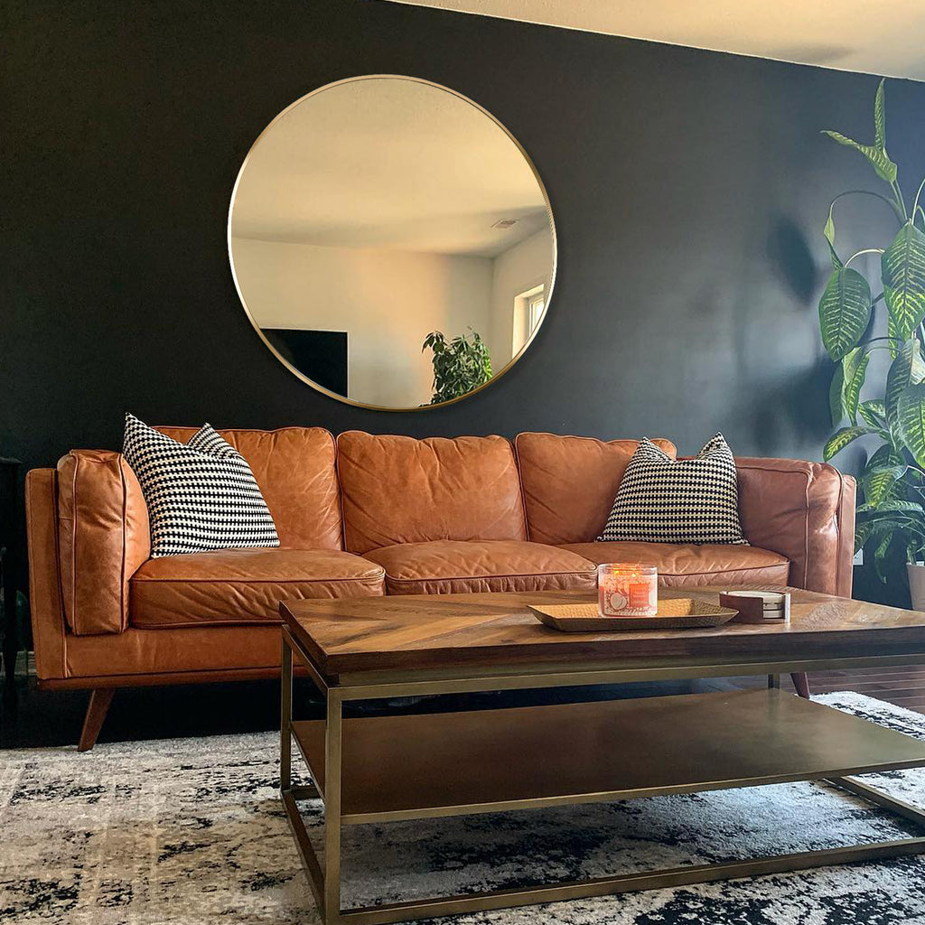 Round gold mirror on a charcoal wall above a cognac leather sofa