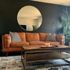 Round gold mirror on a charcoal wall above a cognac leather sofa