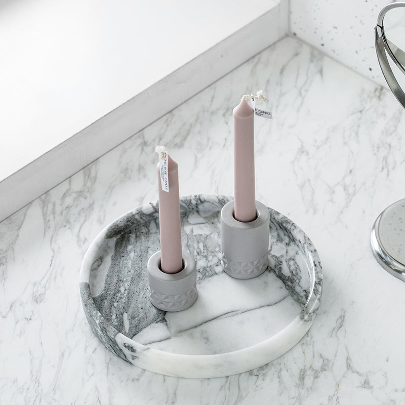 Round white marble tray holding two taper candles in gray holders on a marble counter