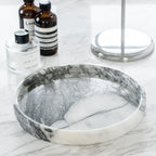 Round marble tray with a raised rim on a marble counter, glass bottles behind