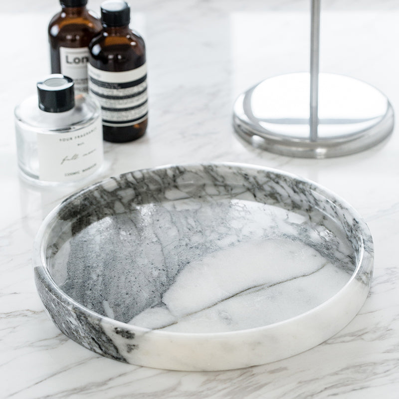 Round marble tray with a raised rim on a marble counter, glass bottles behind