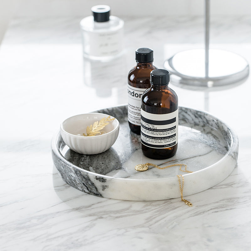 Round white marble tray holding amber bottles, a small bowl and a gold chain