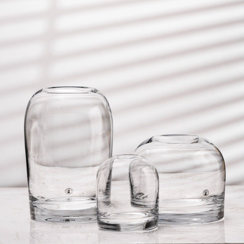 Rounded glass bud vases in clear, three heights side by side on white marble with striped window shadows