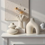 Matte white arch, swirl and fan vases on a white mantel with dried flowers and a small globe