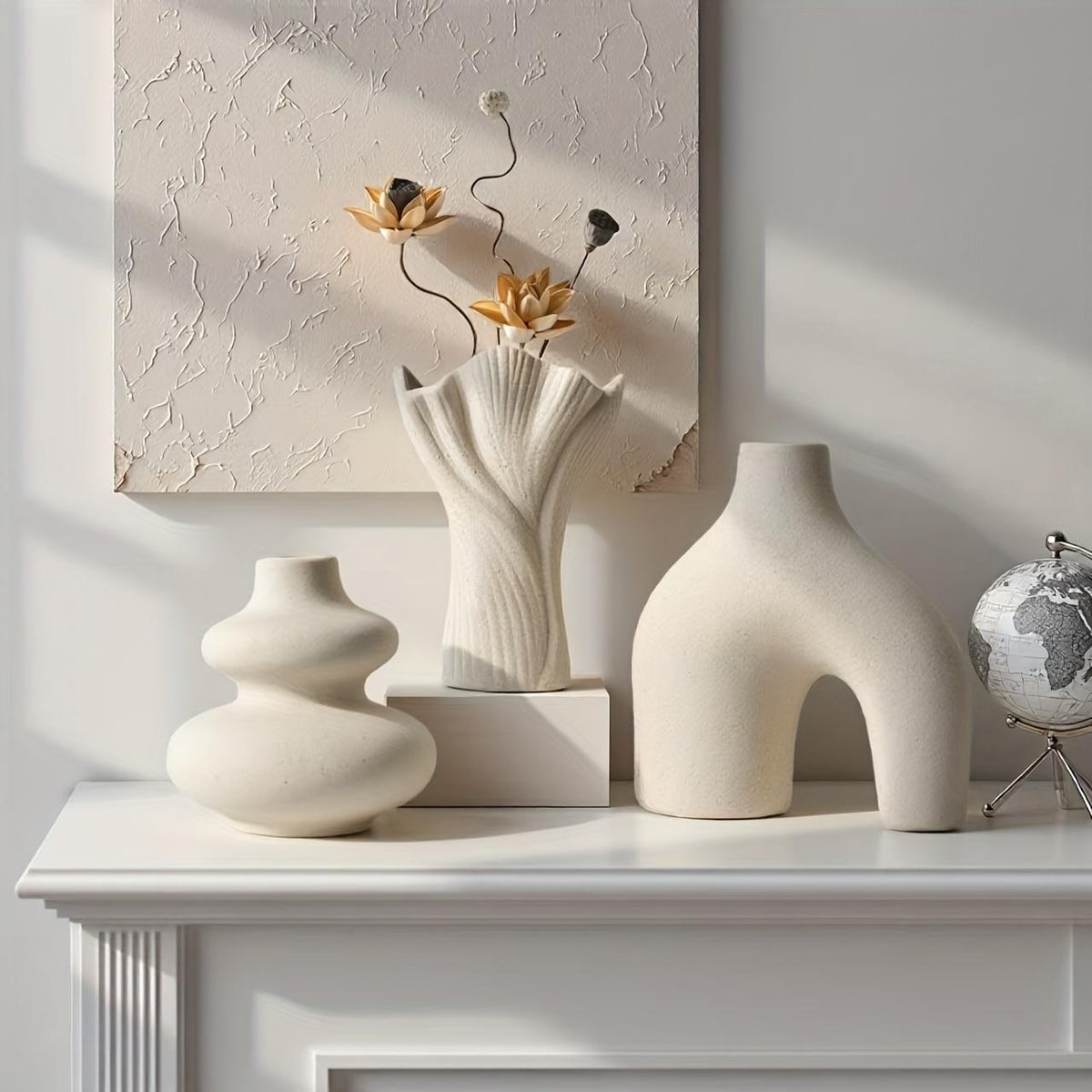 Matte white arch, swirl and fan vases on a white mantel with dried flowers and a small globe
